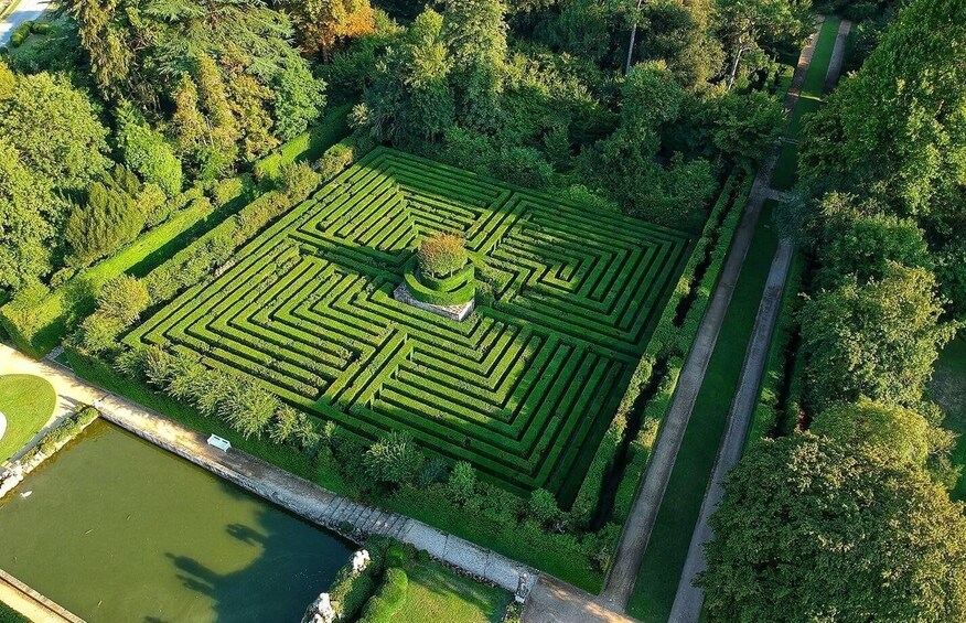 A meticulously designed maze garden with a central circular feature, surrounded by lush greenery and bordered by a waterway. 4