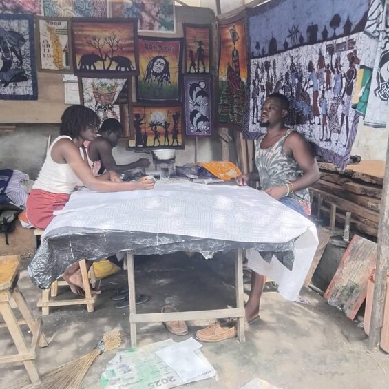 A workshop with people working on a large fabric piece, surrounded by colorful artwork. 1