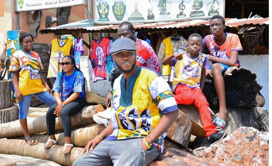 People sitting on logs in front of a shop with colorful jerseys. 2