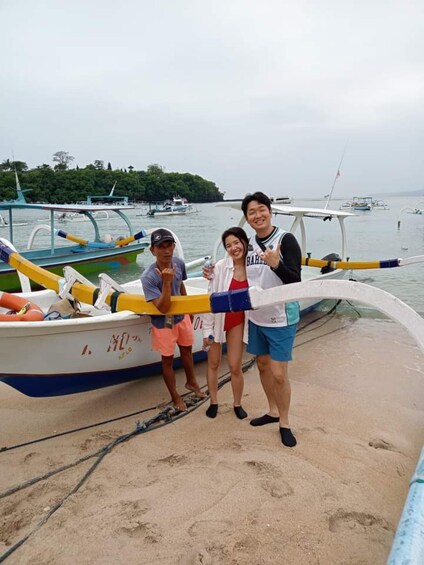 Three people standing on a sandy beach with a boat in the background. 1