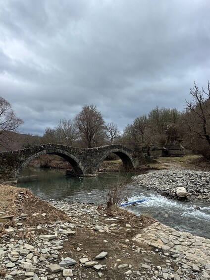 A stone bridge over a river with a rocky riverbank and bare trees in the background. 5