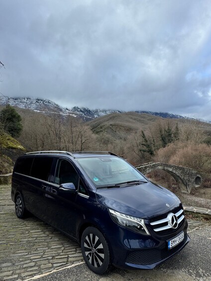 A dark blue Mercedes-Benz minivan parked on a cobblestone path with a mountainous landscape in the background. 4