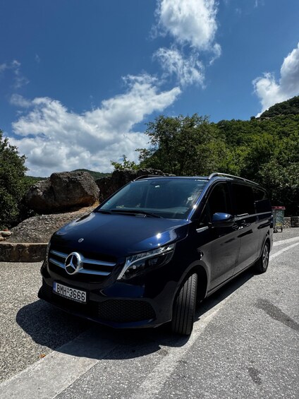 A black Mercedes-Benz SUV parked on a road with a clear sky and greenery in the background. 1