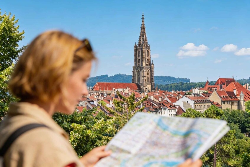 A person holding a map, overlooking a town with a prominent church tower and red-roofed buildings. 2