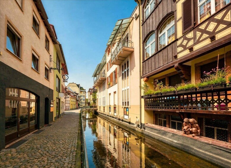 A narrow cobblestone street with buildings on either side, a canal, and a statue of children on the right. 4