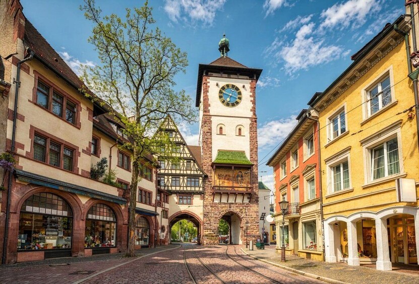 A cobblestone street with a historic clock tower, traditional half-timbered buildings, and a clear blue sky. 5