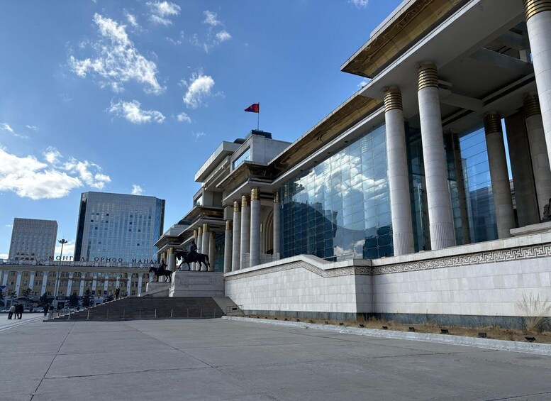 A modern building with large glass windows and classical columns, a flag on top, and a clear blue sky. 2