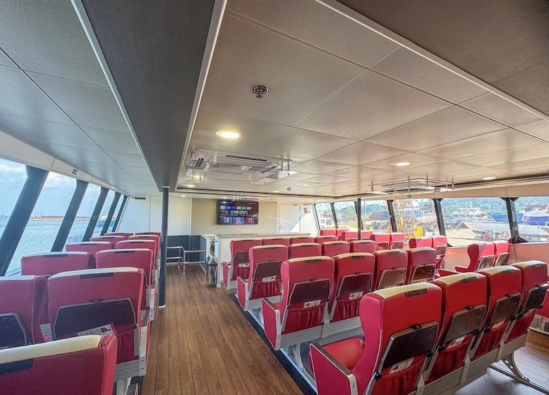 A ferry interior with rows of red seats, a wooden floor, and a screen displaying information. 4