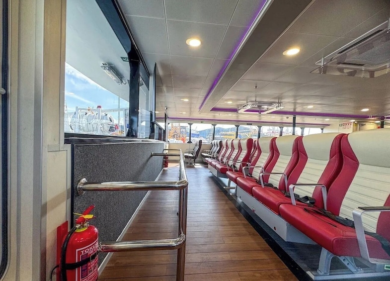 A ferry interior with rows of red and white seats, a fire extinguisher, and a view of the outside through large windows. 2