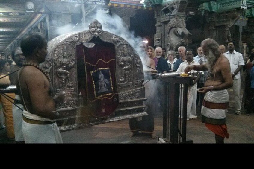 A religious ceremony with ornate temple architecture, a priest performing rituals, and a crowd of onlookers. 2