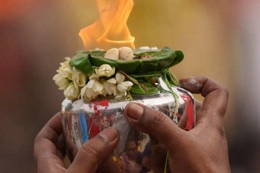 Hands holding a container with a flame on top, containing white flowers and green leaves. 2