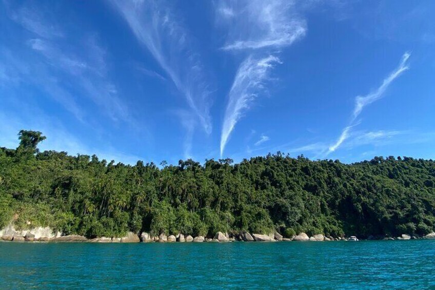 A coastal landscape with a clear blue sky, a forested hill, and calm turquoise waters. 5