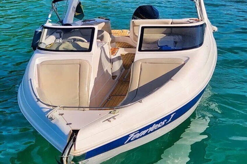 A white boat with a blue stripe and the name 'Tamaris' on the side, floating on clear blue water. 3