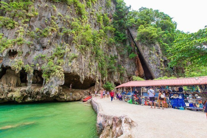A cave entrance with a market and people walking around. 4
