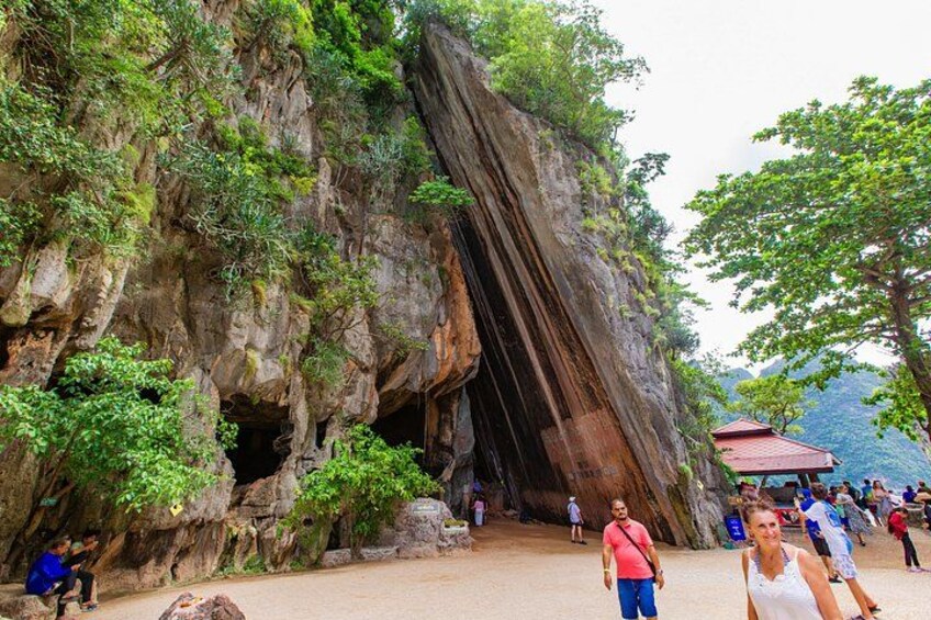 A large rock formation with a cave entrance, surrounded by greenery and a small pavilion. 3