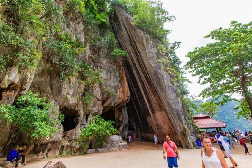 A large rock formation with a cave entrance, surrounded by greenery and a small shelter. 3