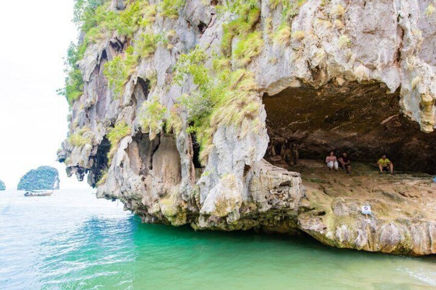 A cave entrance with people inside, surrounded by clear water and rocky cliffs. 5