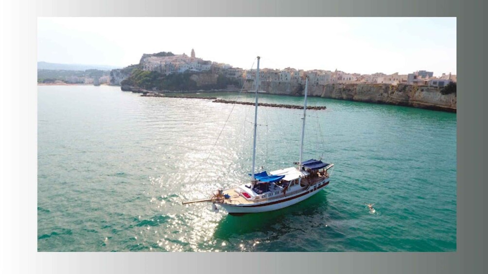 A sailboat on calm turquoise waters, a coastal town with historic buildings, and a prominent cliff. 3