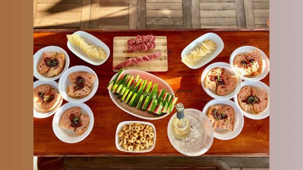 A wooden table with various food items including sliced cucumbers, a jar of pickles, and several plates of sandwiches. 2