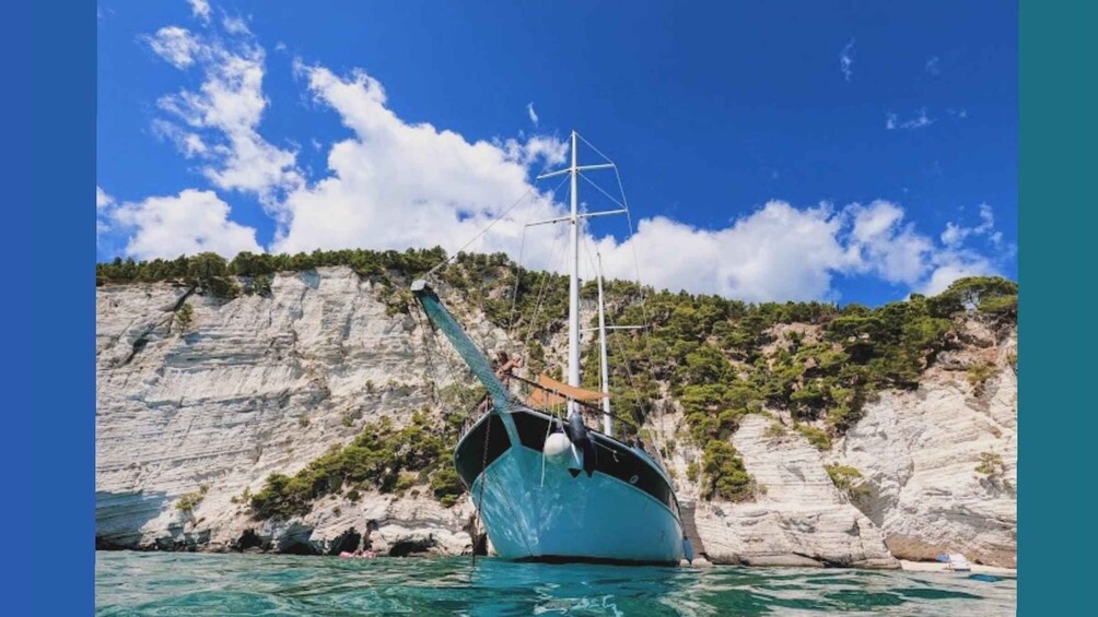 A sailboat anchored near a rocky coastline with cliffs and sparse vegetation. 1