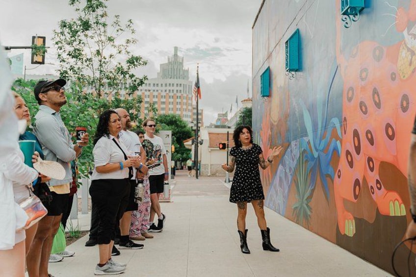 A group of people standing on a sidewalk next to a colorful mural. 3