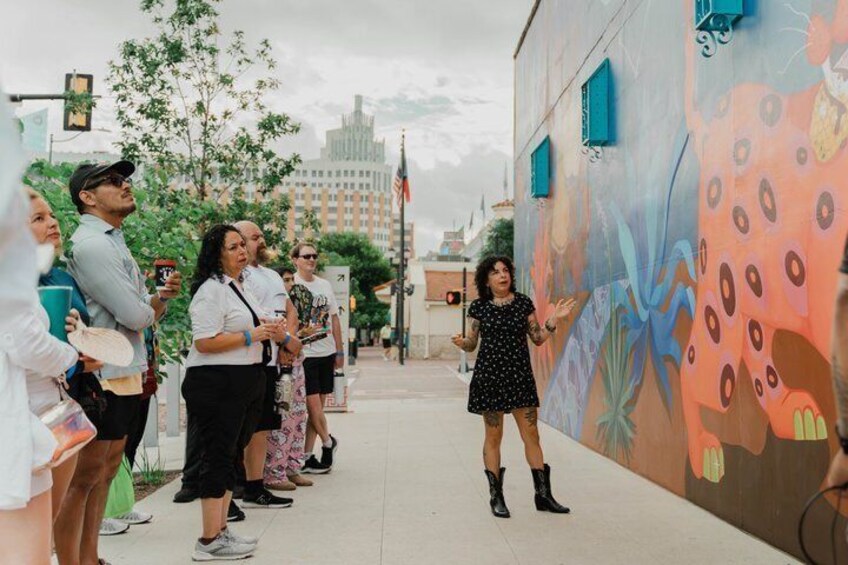 A group of people standing on a sidewalk next to a colorful mural. 3
