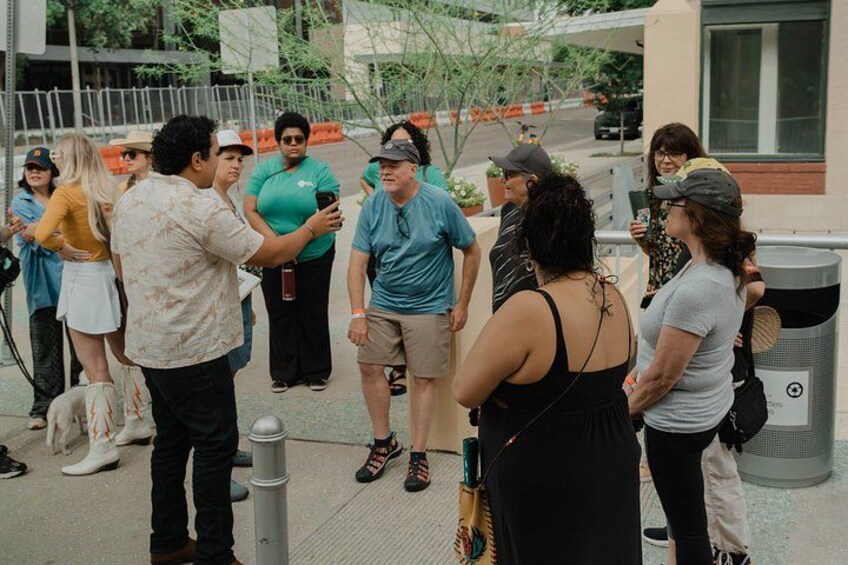 A group of people standing on a sidewalk, some taking photos. 2