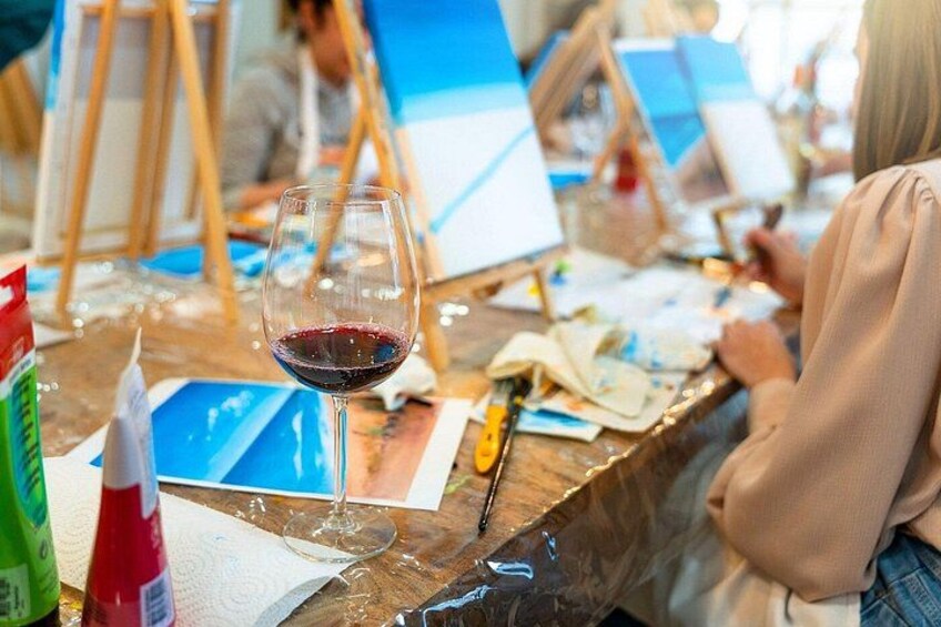 A glass of red wine on a table with art supplies and canvases in an art studio. 2