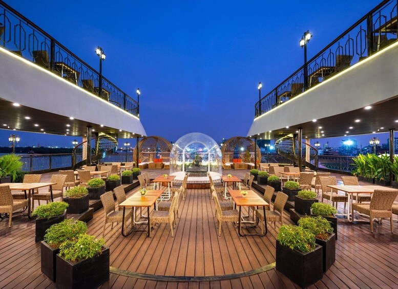 An outdoor dining area with wicker furniture and potted plants, overlooking a cityscape at dusk. 1