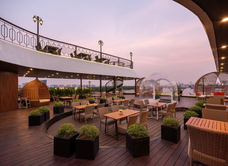 An outdoor café with wooden tables and wicker chairs, surrounded by potted plants. 2