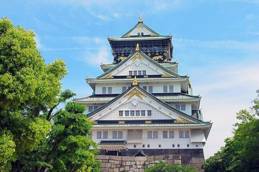 A multi-tiered castle with white walls and green roofs, surrounded by trees. 2