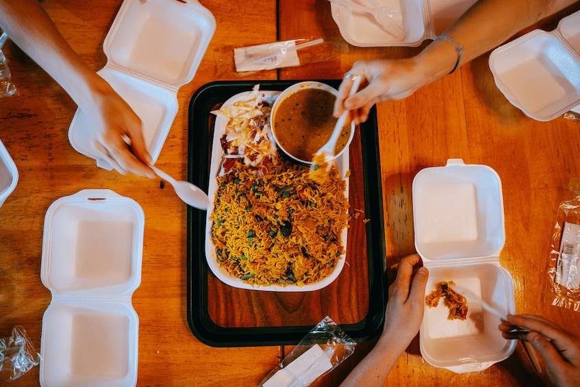 A group of people sharing a meal with rice and a side dish, using disposable utensils and containers. 5