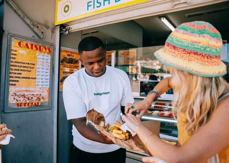 A street food vendor serving a sandwich and fries at a food stall. 1
