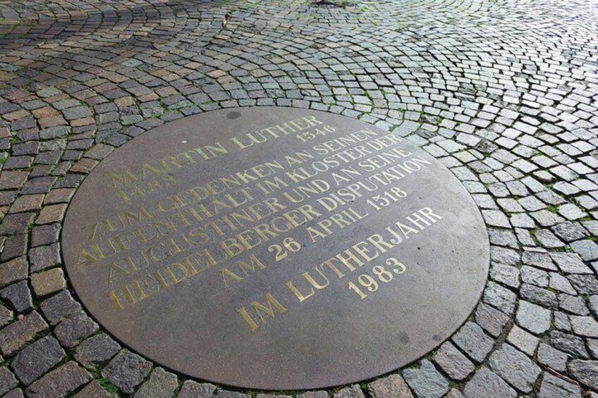 A circular stone plaque with inscriptions, set on a cobblestone pavement. 5