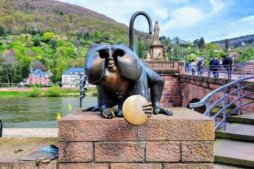 A sculpture of a large animal with a curved neck and a ball on its back, located on a stone platform by a river. 2
