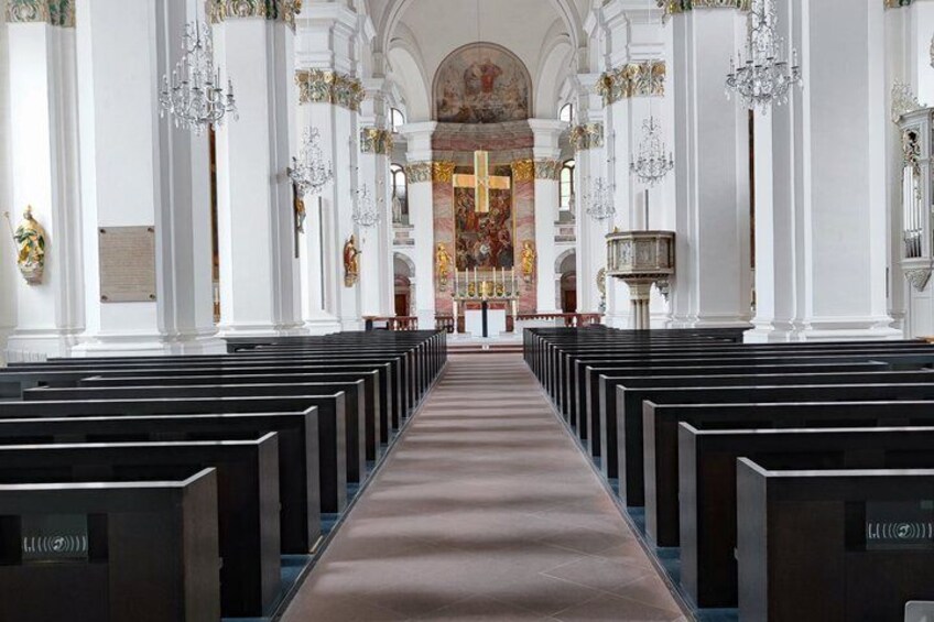 A church interior with rows of pews, a central aisle, and a large altar at the end. 4