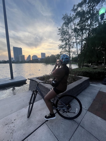 A person on a bicycle by a waterfront with buildings in the background. 2