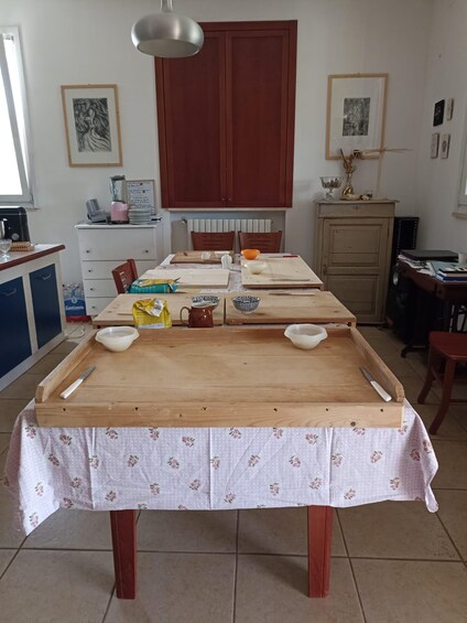 A wooden dining table with a floral tablecloth, surrounded by chairs, in a kitchen with cabinets and a hanging light fixture. 3