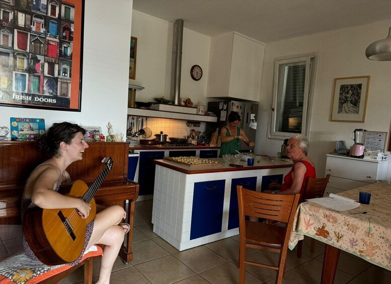 A person playing a guitar in a kitchen with a tiled backsplash, a clock on the wall, and a framed picture of doors. 1