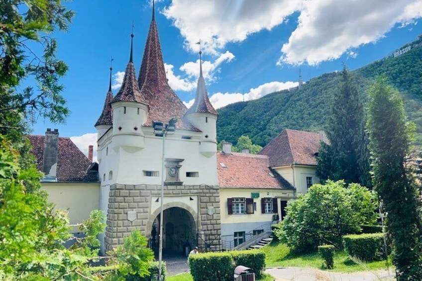 A castle with three spires, surrounded by greenery and a mountain backdrop. 1