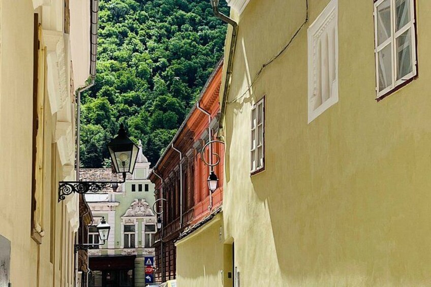 A narrow street with buildings, a lamppost, and a green hill in the background. 2
