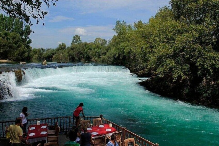 A river with a waterfall, surrounded by trees, and people on a boat. 5
