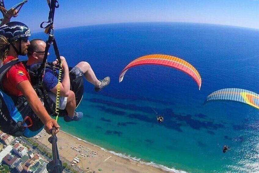 A beach with clear blue waters and people paragliding. 1