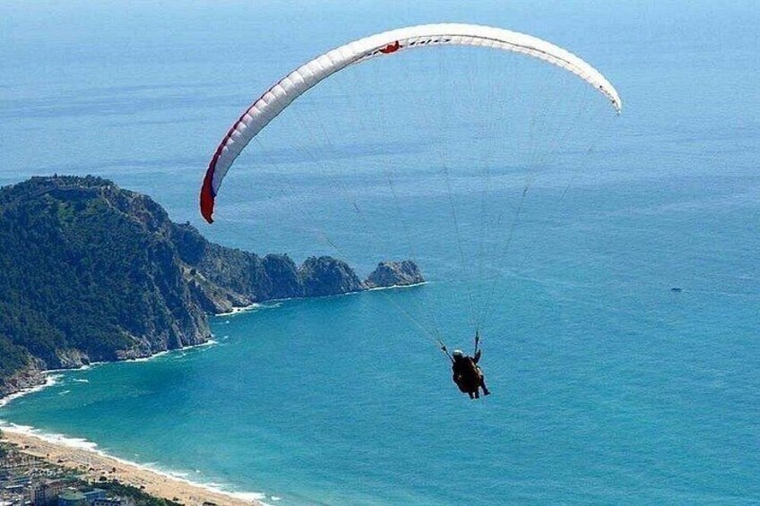 A paraglider flying over a coastal area with a clear view of the coastline and a mountain range in the background. 4