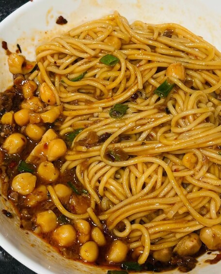 A bowl of noodles with a sauce, chickpeas, and green onions. 2