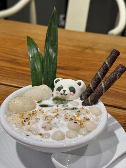 A bowl of dessert with round sweets, a panda decoration, and two sticks. 4