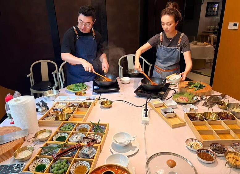 Two people cooking at a table with various ingredients and cooking utensils. 1