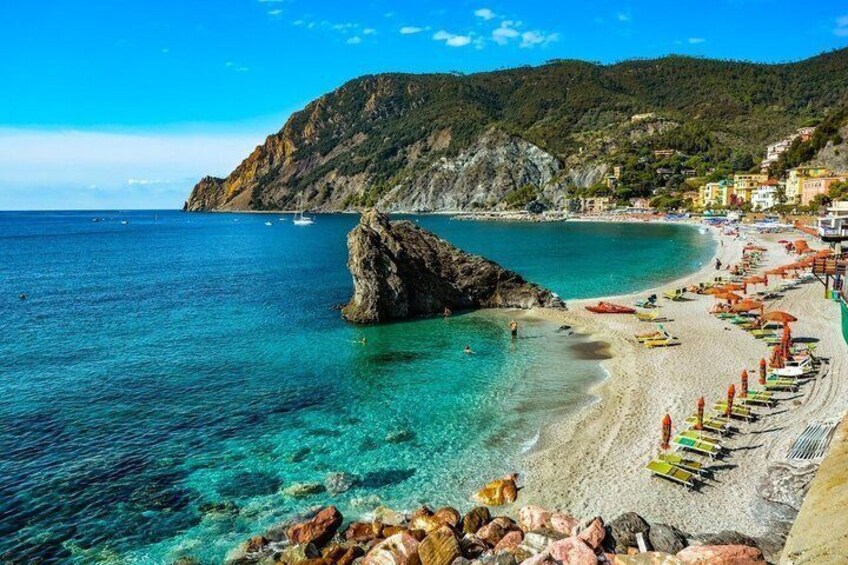 A coastal beach with clear turquoise waters, a rocky outcrop, and colorful umbrellas. 1
