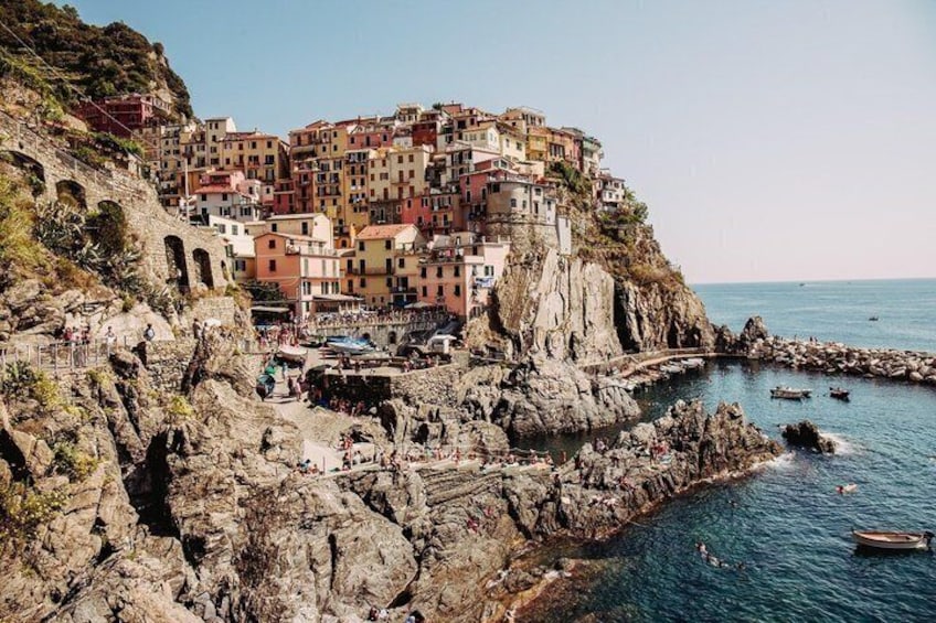 A coastal town with colorful buildings perched on a cliff, rocky shoreline, and boats in the water. 4