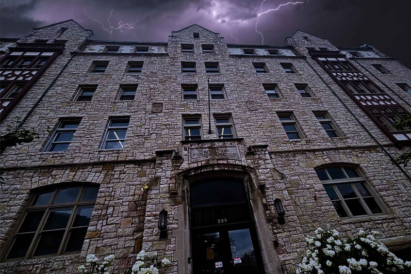 A stone building with a dark entrance and windows, under a stormy sky with lightning. 1
